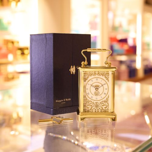 70th Anniversary Carriage Clock from Mappin & Webb, featuring black Presentation box and gold carriage clock with ornatecfold pattern, key to the left of the clock. 