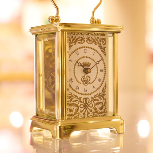 70th Anniversary Carriage Clock from Mappin & Webb, featuring black Presentation box and gold carriage clock with ornatecfold pattern, key to the left of the clock. 