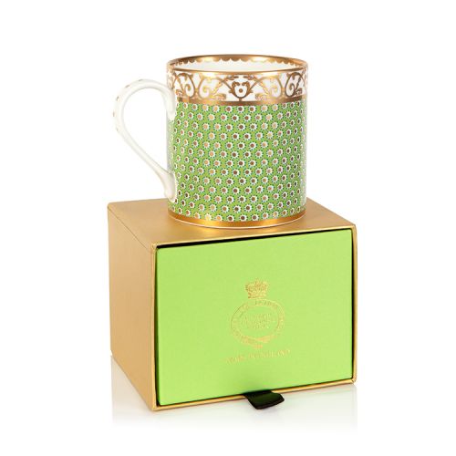 A green mug with gold detailing in a floral design and a white and gold border at the top of the mug
