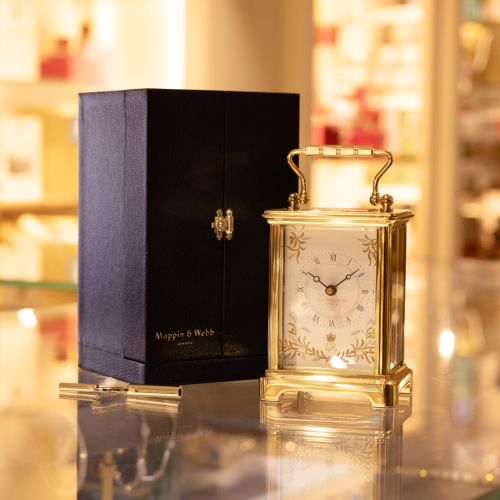 Gold carriage clock with a gold handle and black presentation box.  There is a clock face surrounded by the design of wheat ears and olive branches. On the clock face are the words 'Platinum Jubilee 2022' and an ER surmounted by the crown.