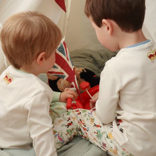 An image of our cotton children's pyjamas suitable for ages between 2 and 7 year-olds featuring blue cuffed pyjama bottoms with a Guards man pattern with trees ,flags and nature. The top features blue cuffs and an illustration of six Guardsmen in uniform