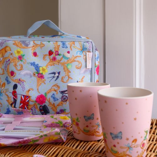 The Picnic on the Palace Lawn, featuring the Summertime Picnic Range with a blue patterned lunch bag and plates with Royal Guards, butterflies, birds and Guardsman and a pink pattern, on a cutlery wrap and cups featuring a royal crown and floral pattern.